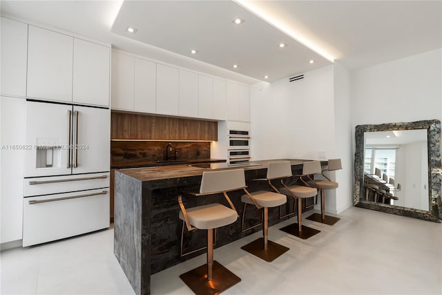 kitchen featuring a breakfast bar, sink, decorative backsplash, white cabinetry, and stainless steel double oven