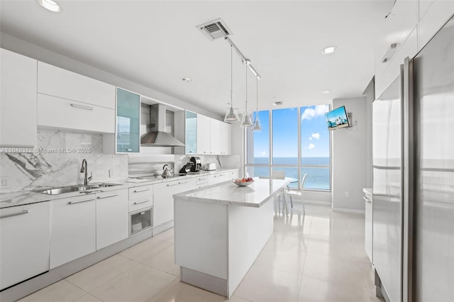 kitchen featuring wall chimney range hood, stainless steel fridge, white cabinets, and a center island