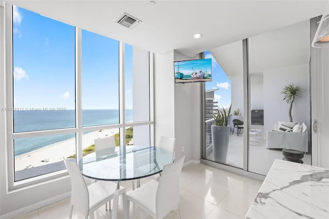 dining space with light tile patterned flooring, a water view, a view of the beach, and visible vents