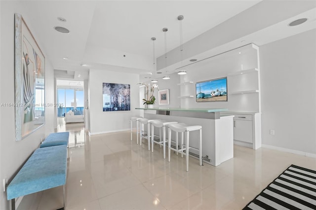 kitchen with white cabinets, a breakfast bar area, a center island, decorative light fixtures, and light countertops