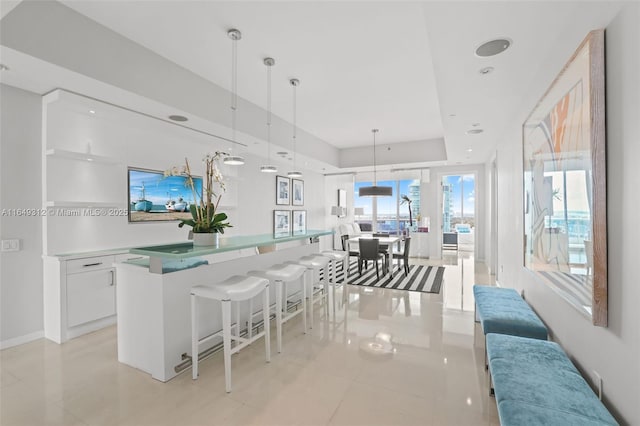 kitchen with a center island with sink, white cabinets, a raised ceiling, a kitchen breakfast bar, and decorative light fixtures