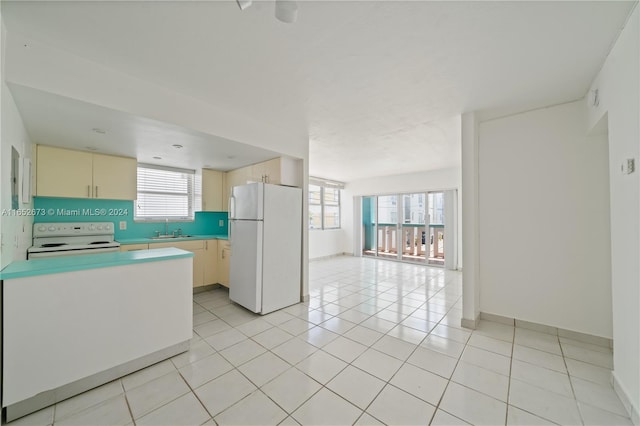 kitchen featuring cream cabinetry, sink, white appliances, and light tile patterned flooring