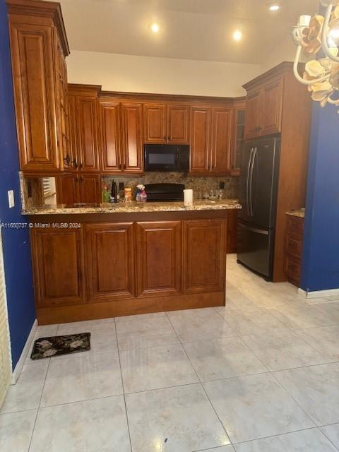 kitchen with light stone counters, black appliances, glass insert cabinets, a notable chandelier, and tasteful backsplash