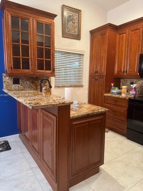 kitchen featuring light stone countertops, a peninsula, black appliances, glass insert cabinets, and backsplash