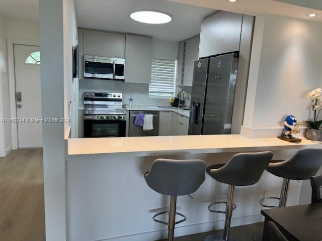 kitchen featuring a kitchen breakfast bar, kitchen peninsula, gray cabinets, stainless steel appliances, and wood-type flooring