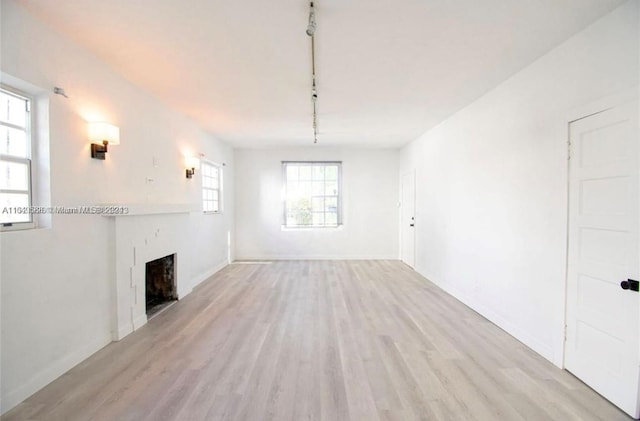 unfurnished living room with a healthy amount of sunlight, rail lighting, and light hardwood / wood-style floors