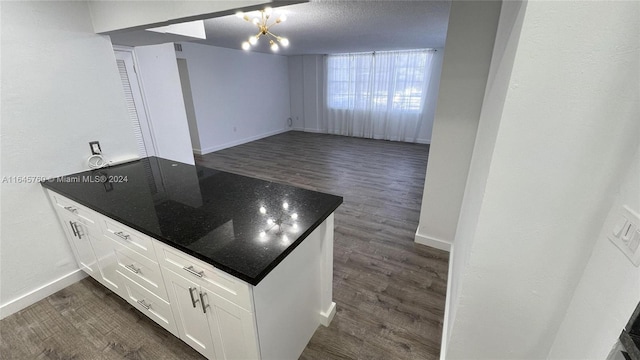 kitchen with dark wood-type flooring, dark stone counters, a chandelier, white cabinetry, and a textured ceiling