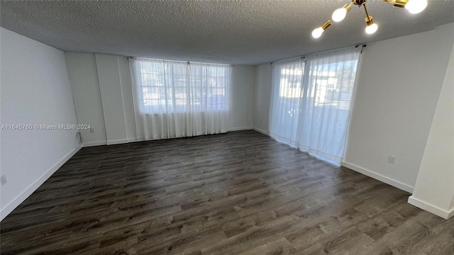 spare room featuring dark wood-type flooring, a healthy amount of sunlight, a textured ceiling, and a chandelier