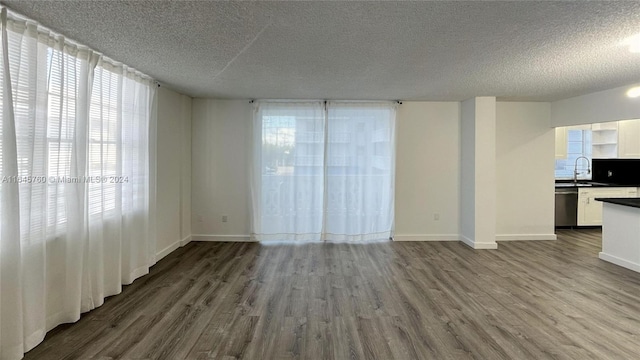 empty room with sink, a textured ceiling, hardwood / wood-style flooring, and a healthy amount of sunlight