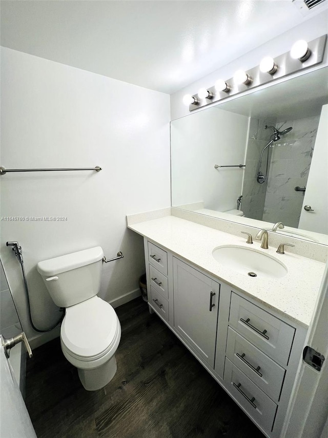 bathroom with vanity, toilet, a tile shower, and wood-type flooring