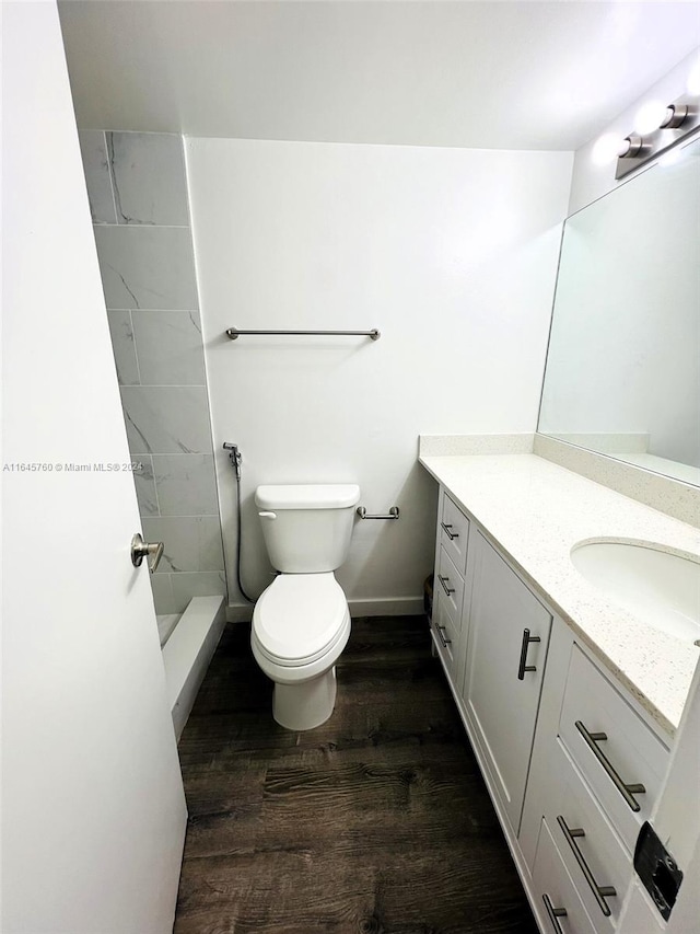 bathroom with vanity, toilet, wood-type flooring, and tiled shower