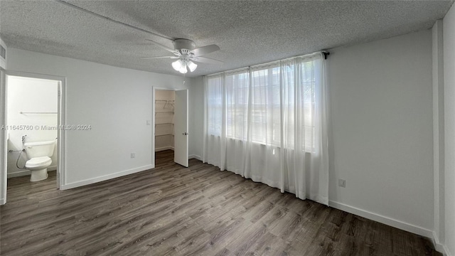 unfurnished bedroom with connected bathroom, a closet, a walk in closet, wood-type flooring, and ceiling fan