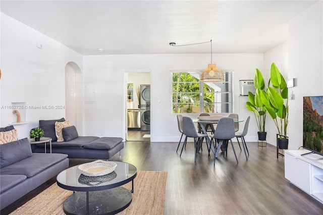 living area with dark wood-style floors, stacked washer and clothes dryer, baseboards, and arched walkways