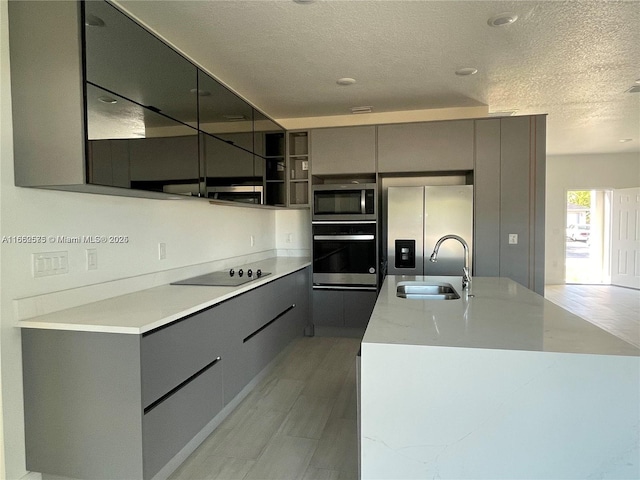 kitchen featuring sink, gray cabinetry, a textured ceiling, an island with sink, and stainless steel appliances