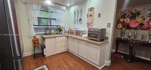 kitchen with white cabinets, a textured wall, light stone counters, freestanding refrigerator, and wood finish floors