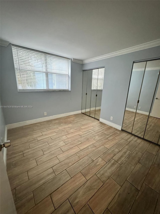 unfurnished bedroom with crown molding, light hardwood / wood-style floors, and multiple closets