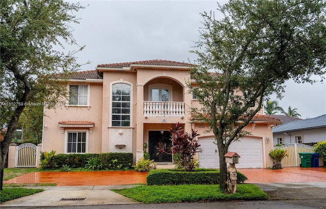 mediterranean / spanish house featuring a balcony, a tile roof, a gate, decorative driveway, and stucco siding