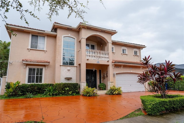 mediterranean / spanish house featuring a balcony, a tiled roof, a garage, and stucco siding