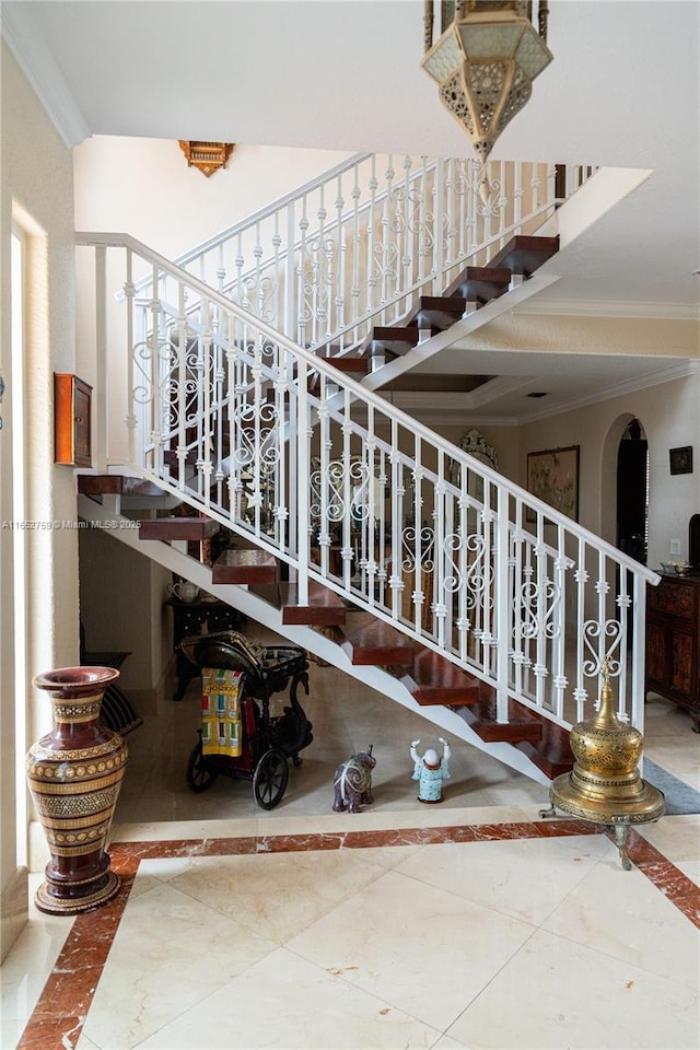 stairs with arched walkways, marble finish floor, and crown molding