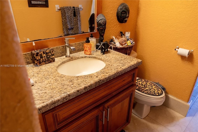 bathroom featuring toilet, a textured wall, and vanity