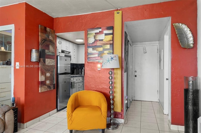 interior space with freestanding refrigerator, white cabinets, light tile patterned flooring, and a textured wall