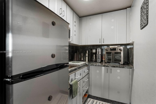 kitchen with freestanding refrigerator, backsplash, white cabinets, and a toaster