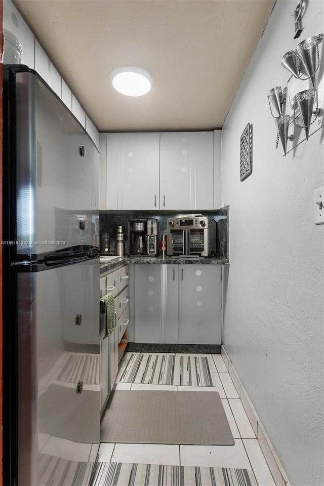 kitchen featuring freestanding refrigerator, dark countertops, white cabinetry, baseboards, and light tile patterned flooring