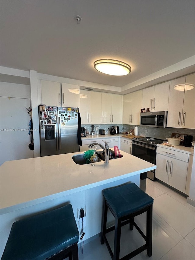 kitchen featuring sink, appliances with stainless steel finishes, light tile patterned flooring, a kitchen bar, and white cabinetry