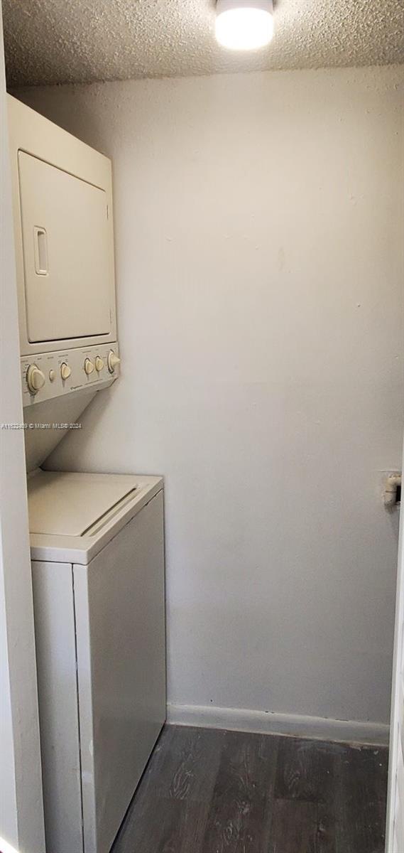 laundry area featuring stacked washer and dryer, dark hardwood / wood-style floors, and a textured ceiling