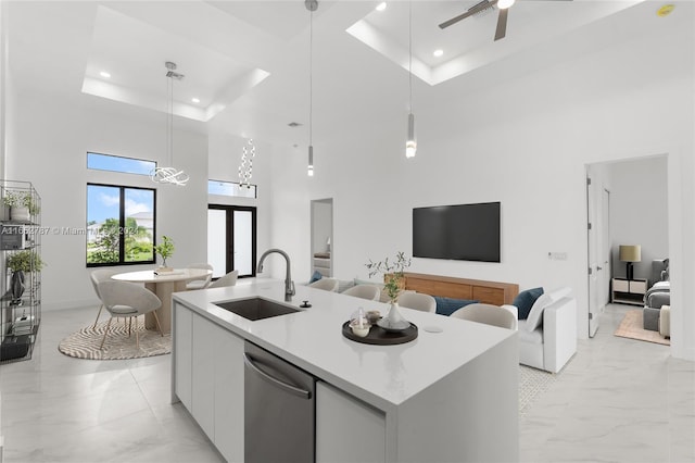 kitchen with decorative light fixtures, a center island with sink, stainless steel dishwasher, sink, and a towering ceiling