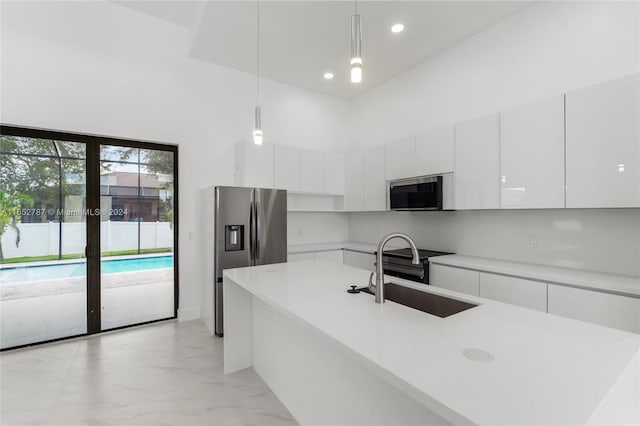 kitchen with decorative light fixtures, stainless steel appliances, sink, white cabinetry, and a towering ceiling