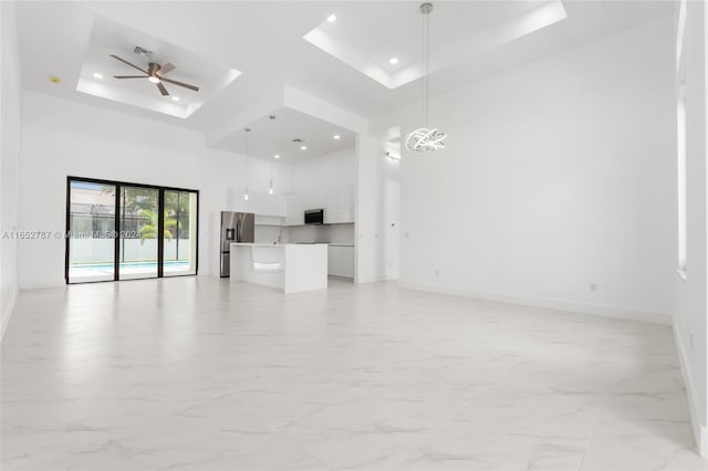 unfurnished living room featuring a raised ceiling, sink, a high ceiling, and ceiling fan