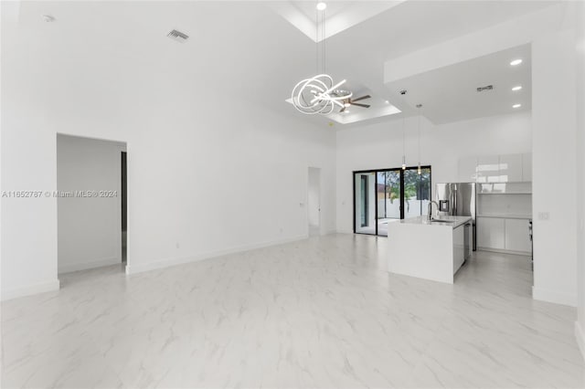 unfurnished living room featuring a high ceiling, a tray ceiling, ceiling fan with notable chandelier, and sink