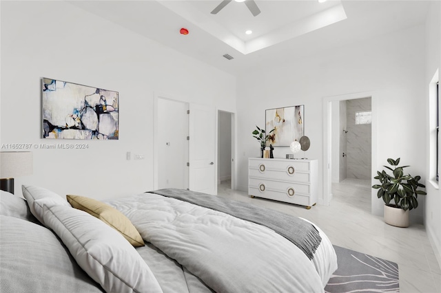 bedroom with ensuite bath, a raised ceiling, and ceiling fan