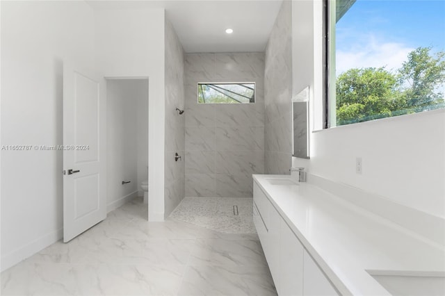 bathroom with toilet, a tile shower, and vanity