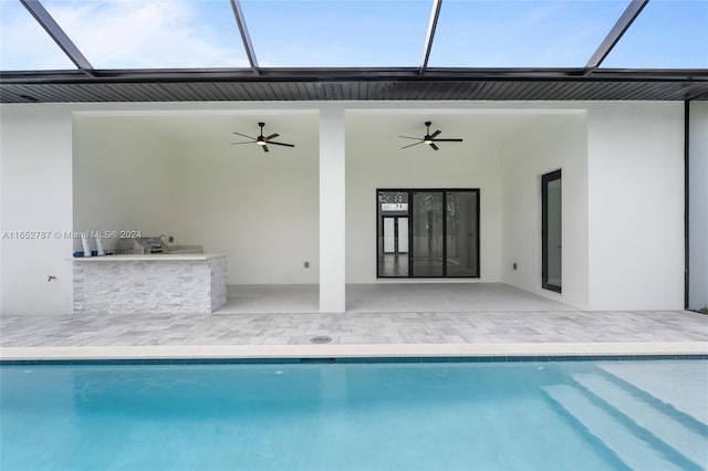 rear view of house featuring glass enclosure, ceiling fan, an outdoor kitchen, and a patio