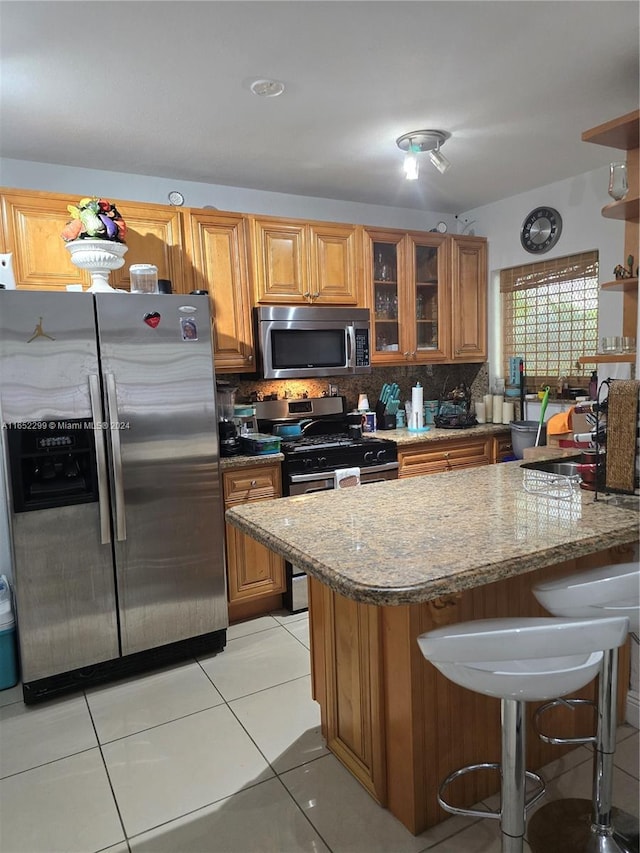 kitchen featuring light stone countertops, light tile patterned floors, tasteful backsplash, a kitchen bar, and stainless steel appliances