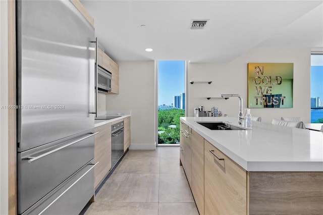 kitchen featuring light tile patterned floors, light brown cabinetry, a center island, sink, and appliances with stainless steel finishes