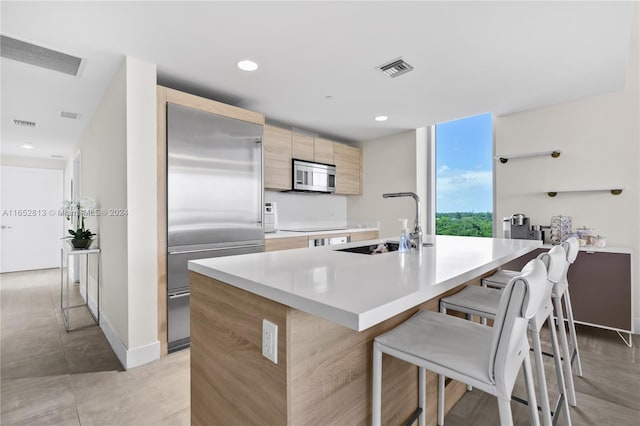 kitchen featuring stainless steel appliances, a kitchen breakfast bar, light brown cabinetry, sink, and a center island with sink