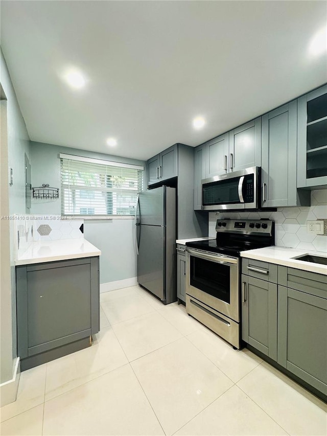 kitchen featuring gray cabinetry, light tile patterned floors, backsplash, appliances with stainless steel finishes, and sink