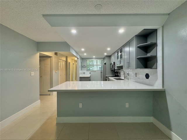 kitchen featuring appliances with stainless steel finishes, sink, kitchen peninsula, light tile patterned flooring, and a textured ceiling