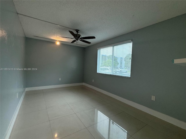 empty room with tile patterned flooring, ceiling fan, and a textured ceiling