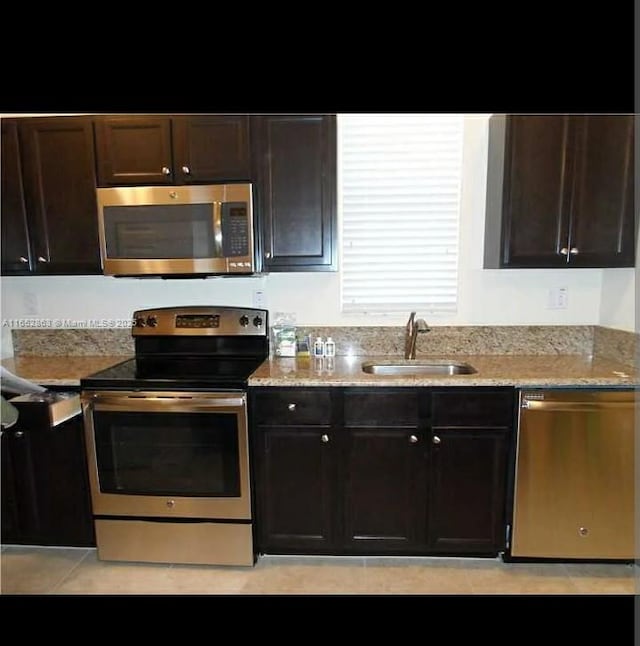 kitchen featuring dark brown cabinets, appliances with stainless steel finishes, sink, light tile patterned floors, and light stone counters