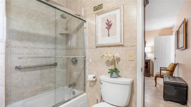 bathroom featuring bath / shower combo with glass door, tile patterned flooring, toilet, a textured ceiling, and tile walls