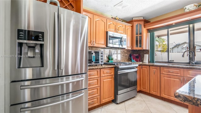 kitchen featuring appliances with stainless steel finishes, dark stone counters, a textured ceiling, sink, and light tile patterned floors