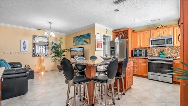 kitchen with backsplash, hanging light fixtures, ornamental molding, appliances with stainless steel finishes, and a breakfast bar area