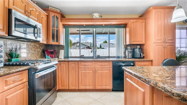 kitchen with dark stone counters, stainless steel appliances, sink, hanging light fixtures, and light tile patterned flooring