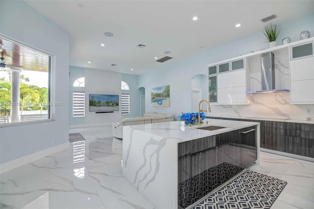 kitchen featuring wall chimney range hood, light stone countertops, white cabinetry, and sink