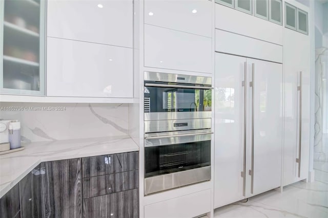 kitchen with stainless steel double oven, tasteful backsplash, light stone counters, and white cabinets