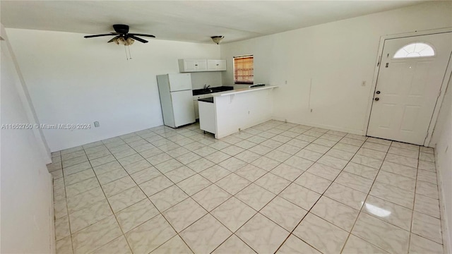 kitchen featuring light tile patterned floors, white refrigerator, white cabinetry, sink, and ceiling fan